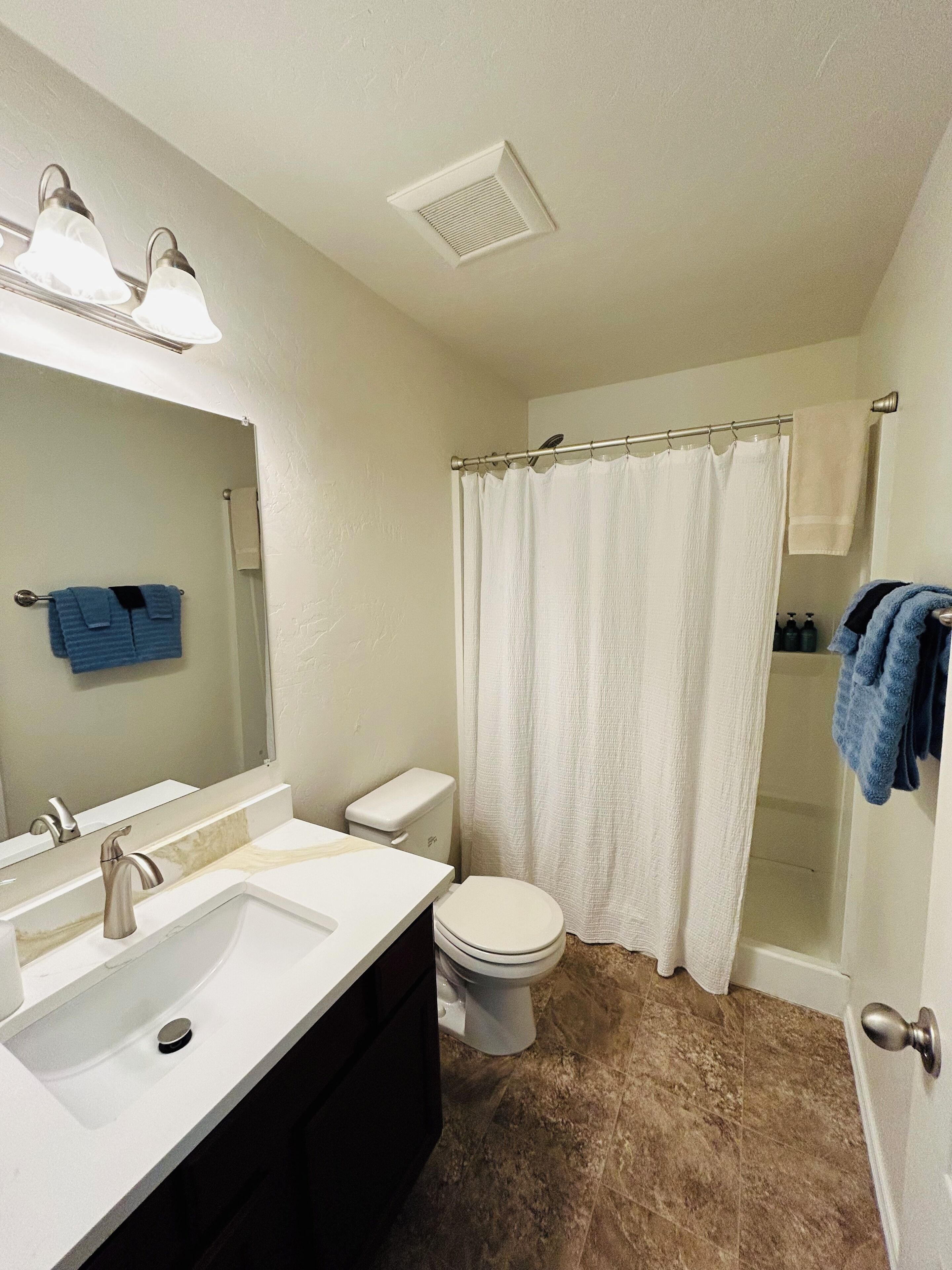 Ein Badezimmer mit weißem Waschbecken, Toilette, Duschvorhang und Handtuchhalter mit blauen Handtüchern.