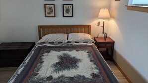 A bedroom with a wooden bed, a nightstand with a lamp, and four framed botanical prints on the wall.