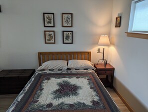 Un dormitorio con una cama de madera, una mesita de noche con lámpara y cuatro láminas botánicas enmarcadas en la pared.