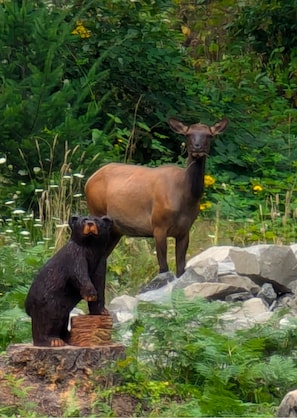 Estatuas de un oso y un ciervo en un entorno natural con rocas y vegetación.