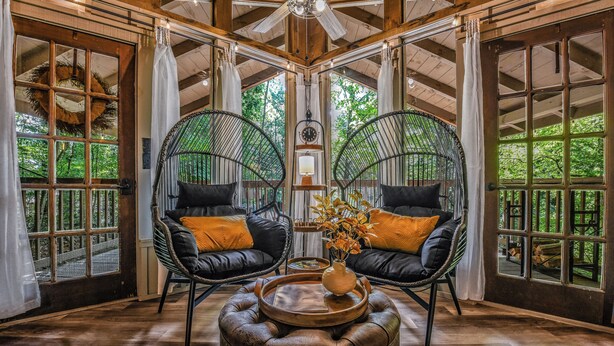 A cozy room with two black leather chairs, a wooden ottoman, and a large window with curtains. - Light'n Bug Bungalow: Pet Friendly, FREE Attraction Tickets, Hot Tub, & Firepit (Townsend)