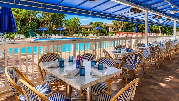 An outdoor pool area with lounge chairs and tables, a pool, and a covered seating area with umbrellas.