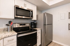 A modern kitchen with stainless steel appliances, including a microwave, oven, and refrigerator, with white cabinetry and a granite countertop. - Park Shore Resort- BLDG I #351*Remodeled* (Park Shore Resort)