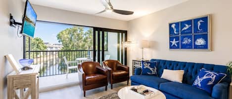 Una sala de estar con un sofá azul, dos sillones de cuero, una mesa de centro, un televisor y un balcón con vistas.