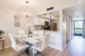 Een moderne keuken met roestvrijstalen apparatuur, een eetgedeelte met witte stoelen en een kroonluchter.