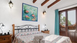 A bedroom with a bed, a painting, two wall-mounted lamps, a wooden nightstand, and a wooden wardrobe.