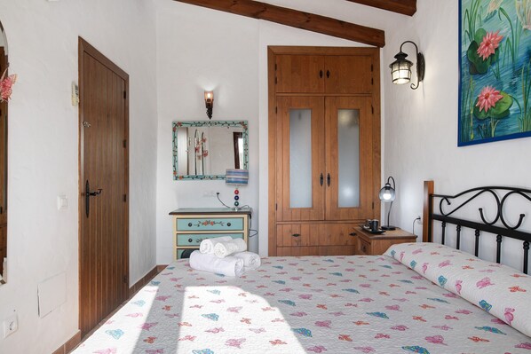 A bedroom with a bed, wooden wardrobe, a dresser, a mirror, and a wall-mounted lamp. - Holiday Home 'Casa Rural La Higuera' with Shared Pool, Wi-Fi and Air Conditioning (Barbate)