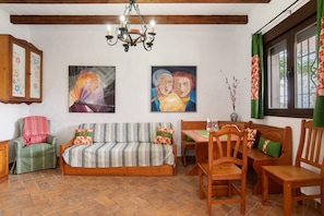 A cozy room with a wooden sofa, a dining table with chairs, a chandelier, and artwork on the walls. - Holiday Home 'Casa Rural La Higuera' with Shared Pool, Wi-Fi and Air Conditioning (Barbate)