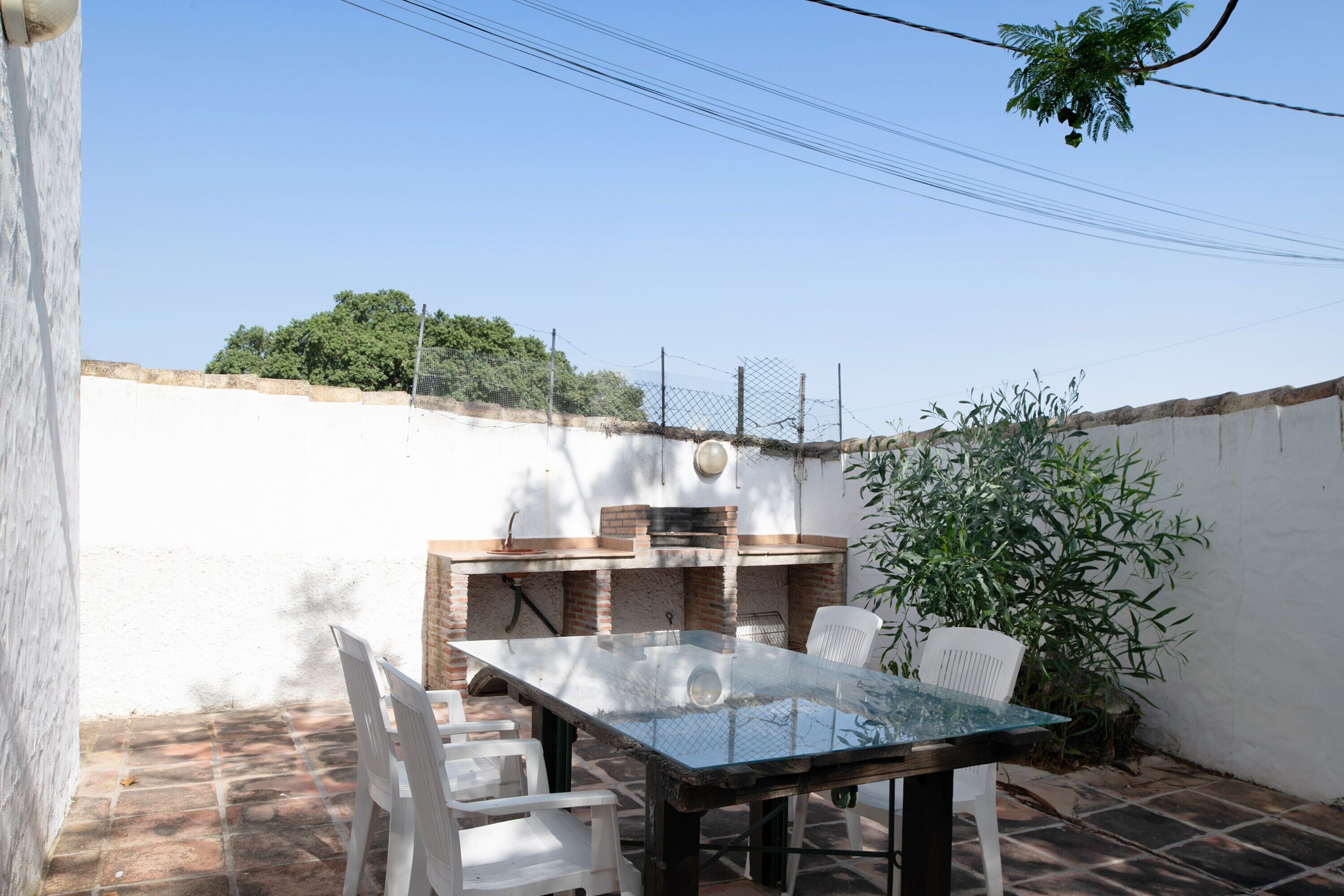 Un patio con una mesa, sillas, una parrilla de barbacoa y una pared blanca.