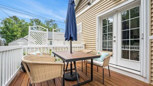 A wooden deck with a table and chairs, a covered umbrella, and a white fence.