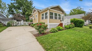 A two-story house with a front porch, a small garden with flowers, and a clear blue sky.