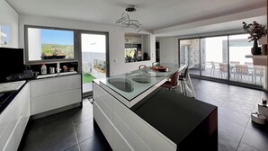 A modern kitchen with a glass island, a dining area with a glass table, and a view of a balcony with outdoor furniture. - Da Serra Guest House (Azeitão)