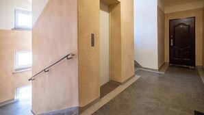 Un corridoio con parete beige dalla texture materica, ringhiera in metallo, una porta con placca numerica e una finestra.