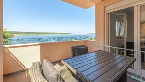 Un balcón con vista al mar, mobiliario de mimbre y una puerta de cristal que da a un espacio interior.