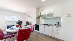 Una cocina moderna con armarios blancos, un comedor con sillas rojas y vistas al exterior a través de una ventana.