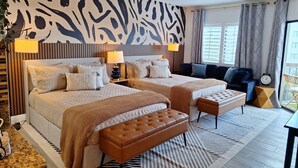 Ein Hotelzimmer mit zwei Betten, einem Schlafsofa, einer Bank, einem großen Fenster und einer zebrastreifenartigen Wand.