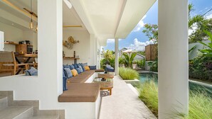 A modern outdoor living area with a sofa, coffee table, and steps leading to a covered patio. - Villa Palikua (Tabanan)
