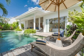 Ein moderner Poolbereich mit Liegestühlen, einer Holzterrasse und einem großen Sonnenschirm.