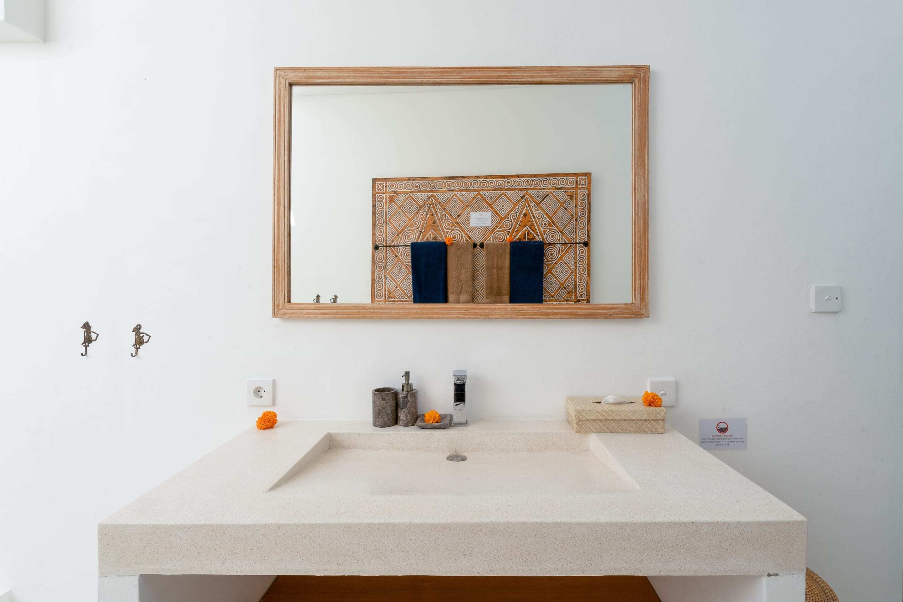 A bathroom with a large rectangular sink, a mirror with a geometric frame, and a small decorative item on the wall.