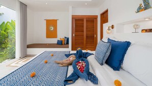 A modern bedroom with a large bed, a sofa, and a view of greenery outside. - Villa Palikua (Tabanan)