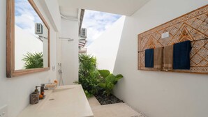 Une salle de bain moderne avec un grand miroir, un lavabo et une douche. On y trouve également des plantes et un motif décoratif sur le mur.