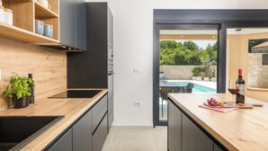 A modern kitchen with wooden shelves, a built-in oven, and a view of a pool.