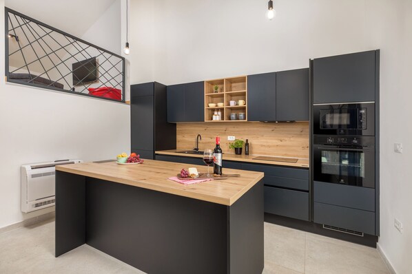 Une cuisine moderne dotée d’un îlot central, de meubles de couleur noire, d’un plan de travail en bois et d’étagères intégrées.