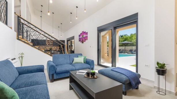 A modern living room with a staircase, a pool view, and a large window.