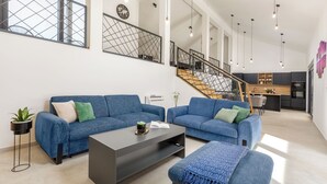 A modern living room with two blue sofas, a coffee table, and a staircase leading to a kitchen.