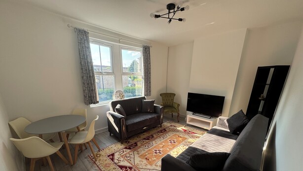 En moderne stue med sofa, stole, fjernsyn og et mønstret tæppe.