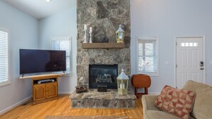 Una sala de estar con chimenea de piedra, televisor de pantalla plana, mueble de entretenimiento de madera y sofá color beige.