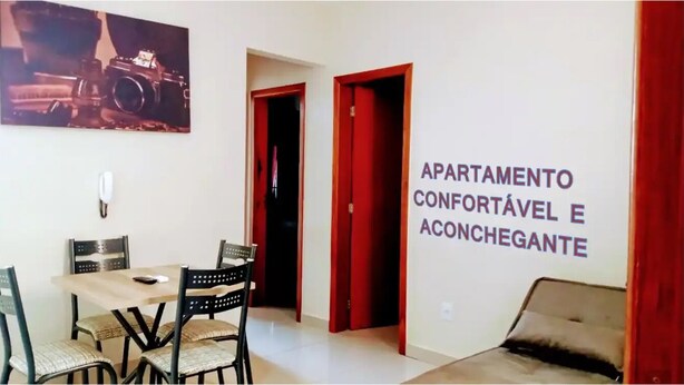 A dining area with a table and chairs, a painting on the wall, and a sign indicating the apartment is comfortable and welcoming.