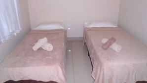 Two single beds with pink bedding and rolled towels, a white wall, and a window with white curtains.