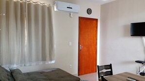 A room with a bed, a wooden door, a television mounted on the wall, and an air conditioning unit.