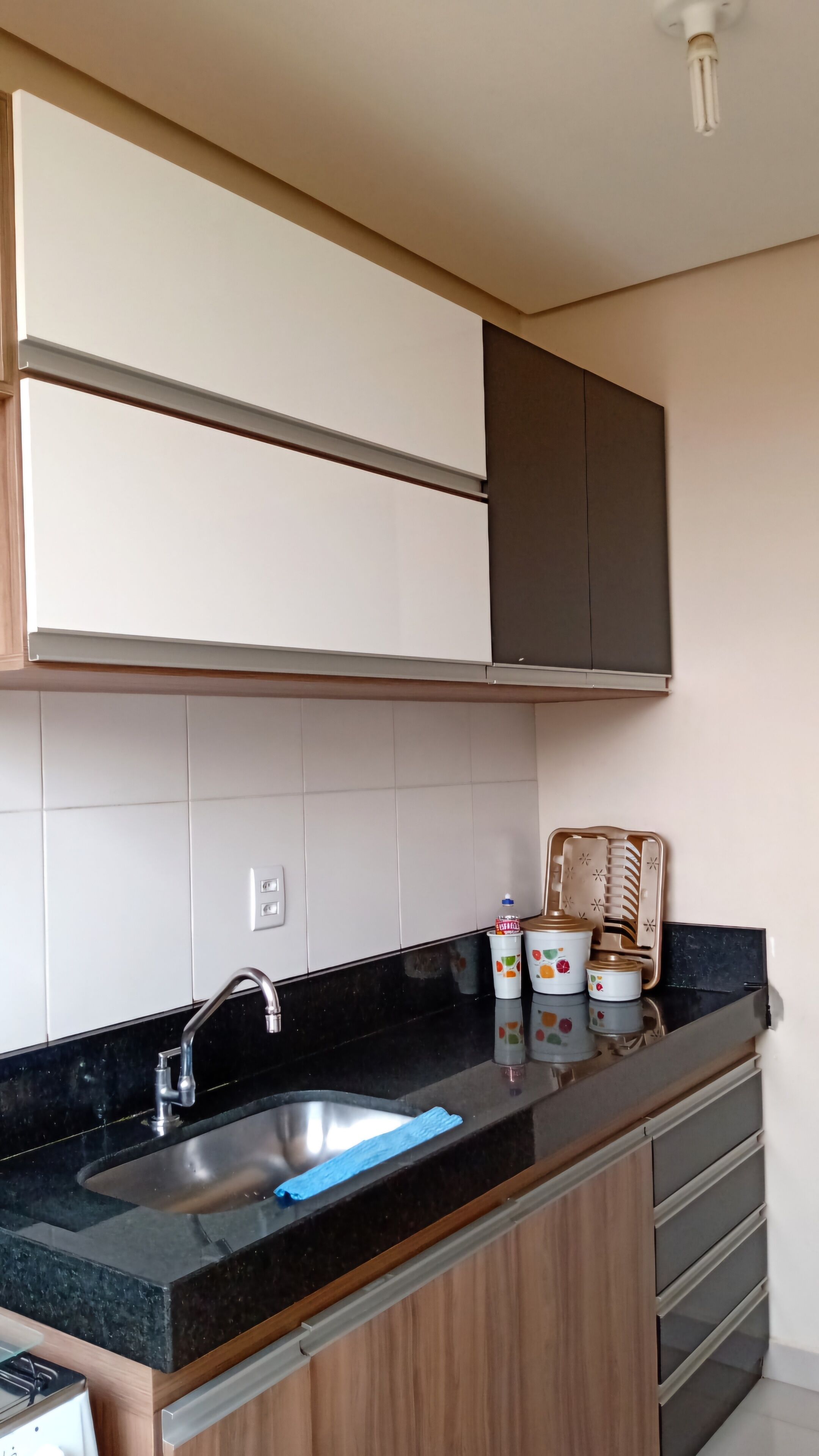 Cozinha com bancada preta, pia de aço inoxidável e armários de madeira.