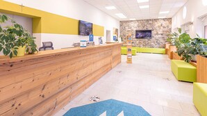 A reception area with a wooden reception desk, a stone wall, and green seating. - Amazing Apartment in Styria With Balcony (Eisenerz)