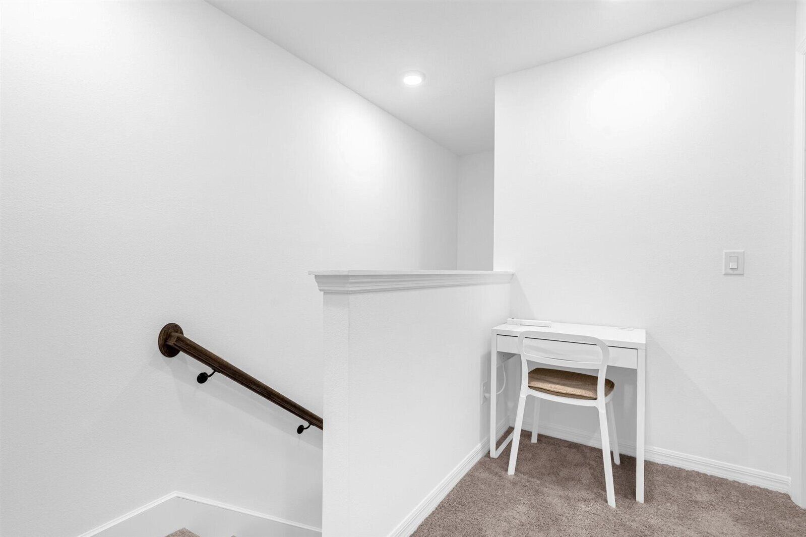 A white room with a staircase, a white desk, and a chair.