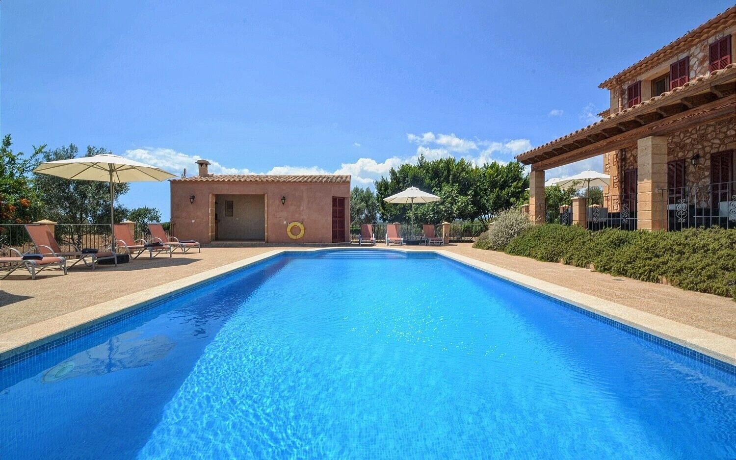 A swimming pool with lounge chairs and umbrellas, surrounded by stone buildings.