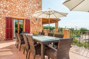 A stone building with a glass table and wicker chairs, a balcony with a railing, and a view of greenery. - Country House 'Can Pedro - Sa Torre Nova' with Sea View, Wi-Fi and Air Conditioning (San Llorenç de Cardessar)