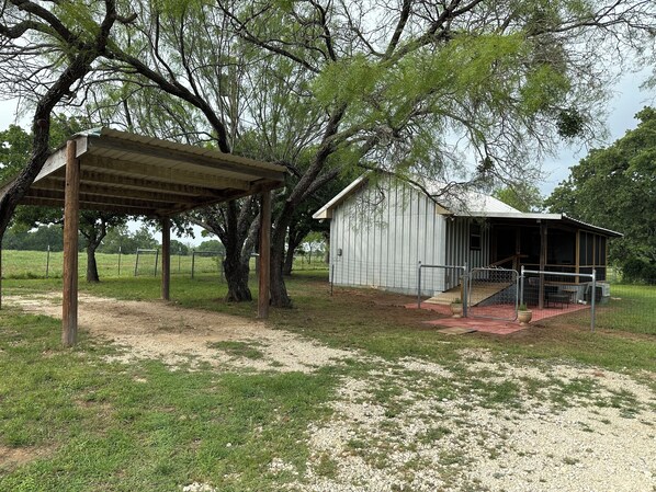 A rustic barn with a covered porch and a fenced area with trees.