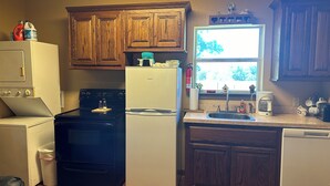 A kitchen with wooden cabinets, a stove, a refrigerator, a dishwasher, and a window with a view of trees. - Cozy cabin in Glen Rose with AC, WiFi, Close to all major attractions! (Glen Rose)