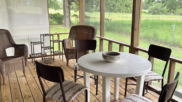 A covered outdoor seating area with a round table and chairs, overlooking a grassy field. - Cozy cabin in Glen Rose with AC, WiFi, Close to all major attractions! (Glen Rose)