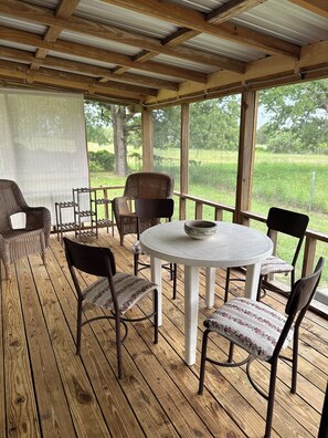 Un espace extérieur abrité, avec une table ronde et des chaises, donnant sur un champ verdoyant.