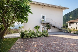 Um edifício moderno com um pátio pavimentado em pedra, uma escadaria e uma varanda.