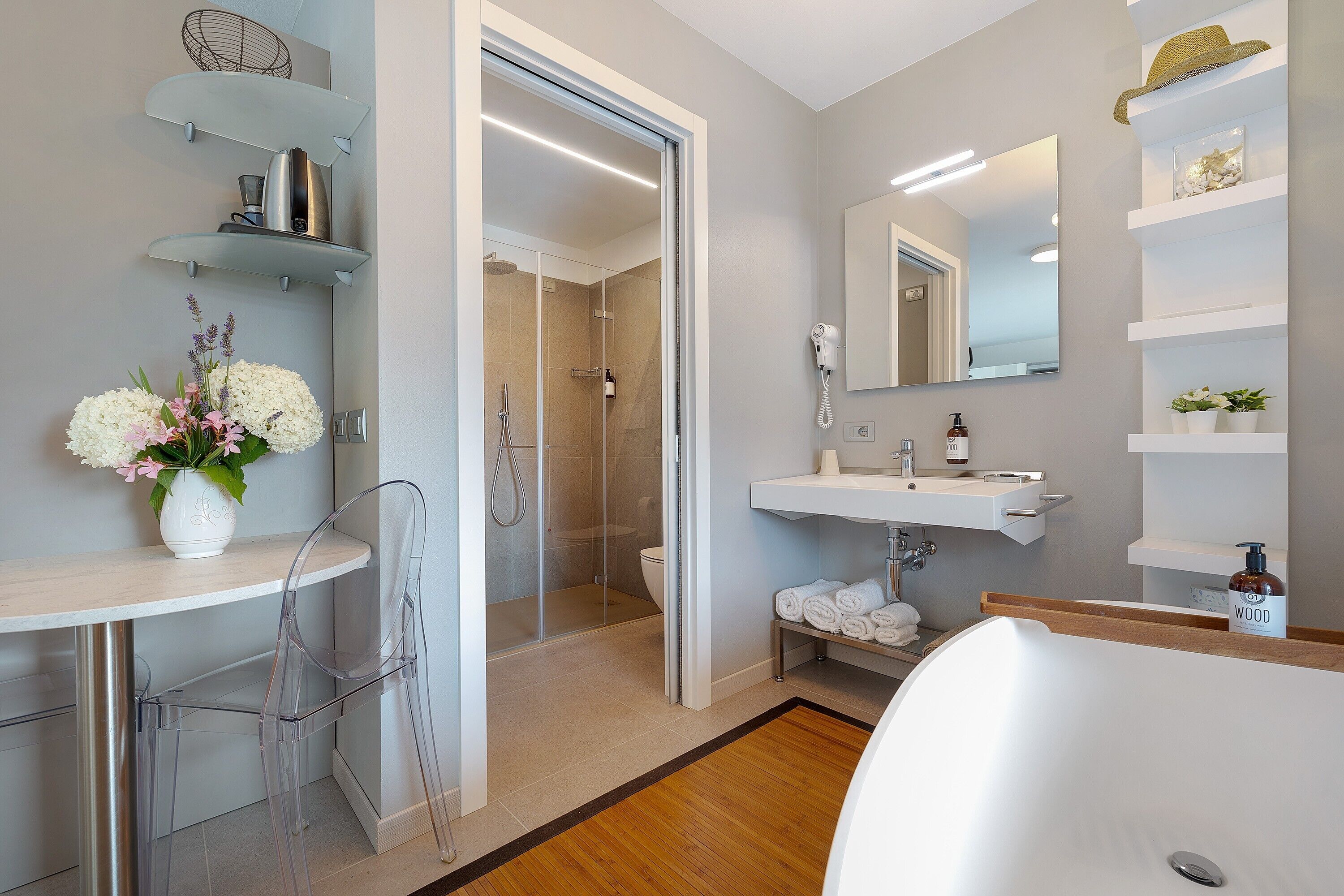 Een moderne badkamer met douche, toilet en wastafel. Er zijn planken met toiletartikelen en een bloevas.