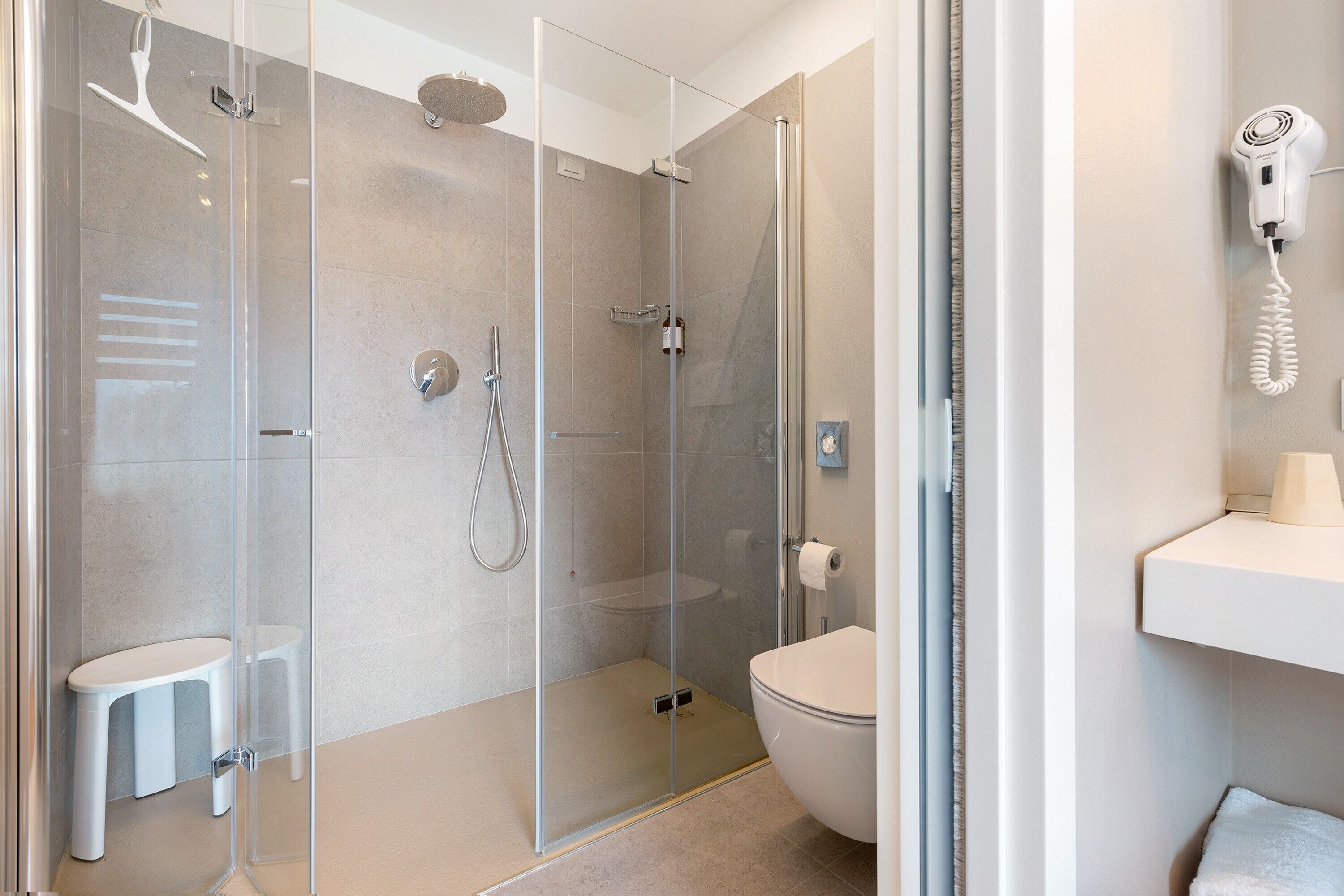 A modern bathroom with a glass-enclosed shower, a toilet, and a hairdryer mounted on the wall.