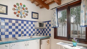 Una cocina con salpicadero de azulejos, microondas, lavamanos y ventana con cortina.