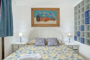 Une chambre à coucher comprenant un lit, deux tables de chevet, une tête de lit, un tableau accroché au mur et un mur recouvert de carreaux.