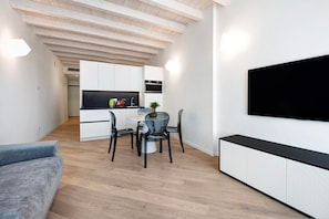 En moderne opholdsstue med spiseplads, køkken og et fladskærms-tv på væggen.