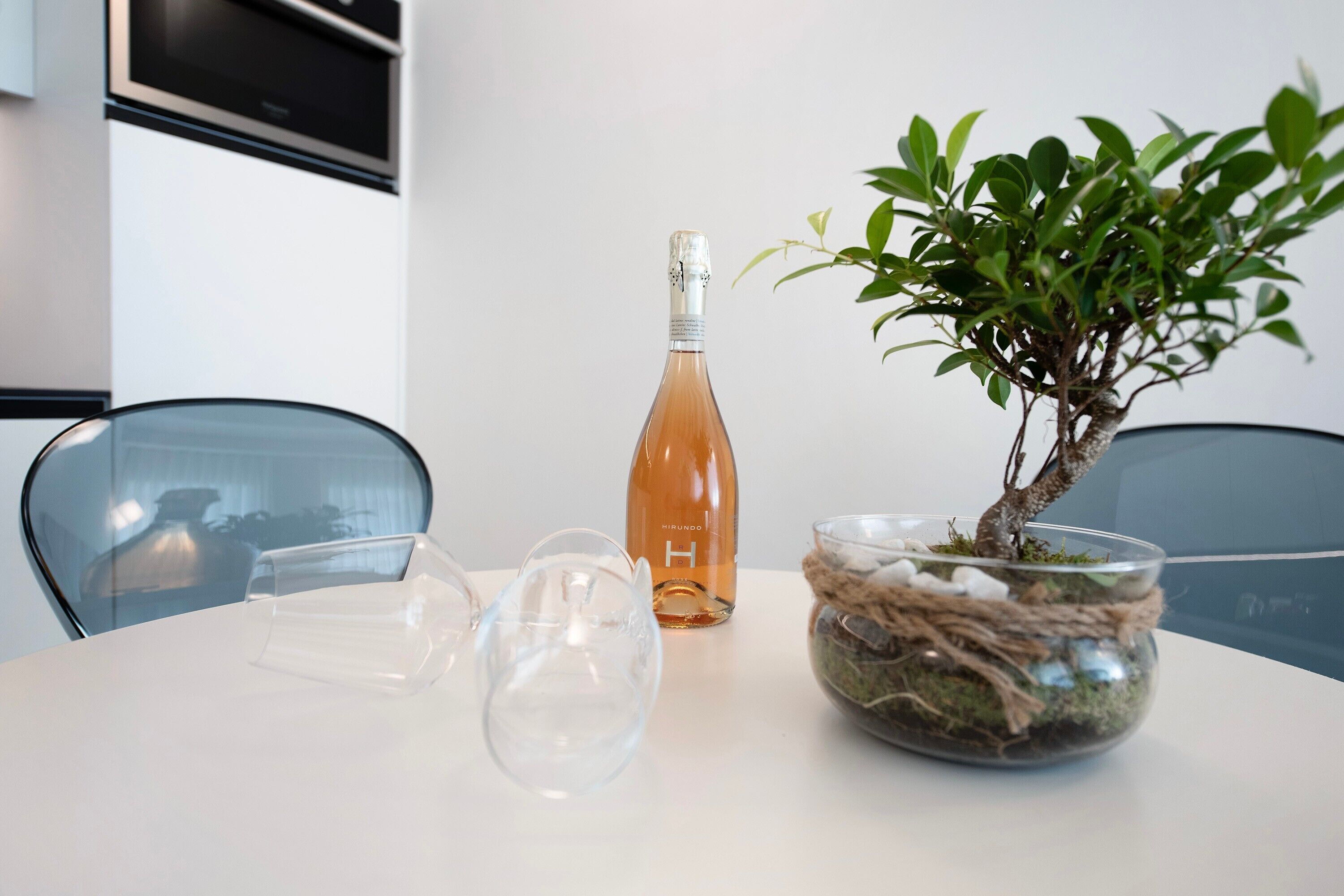 A table with a bottle, a bonsai tree, and a glass bowl.